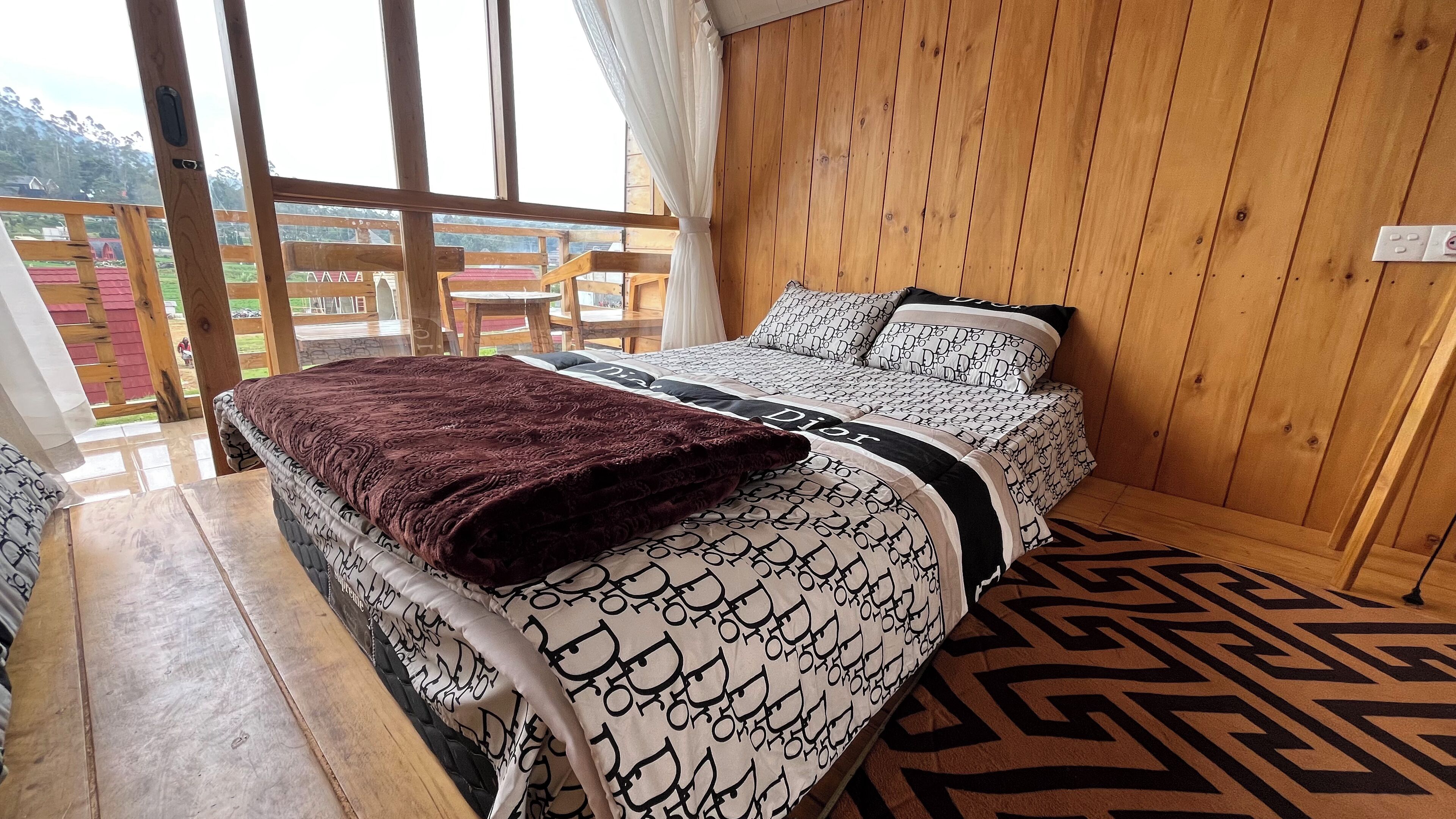 Un dormitorio con cama, piso de madera, ventana con cortinas y vistas al exterior.