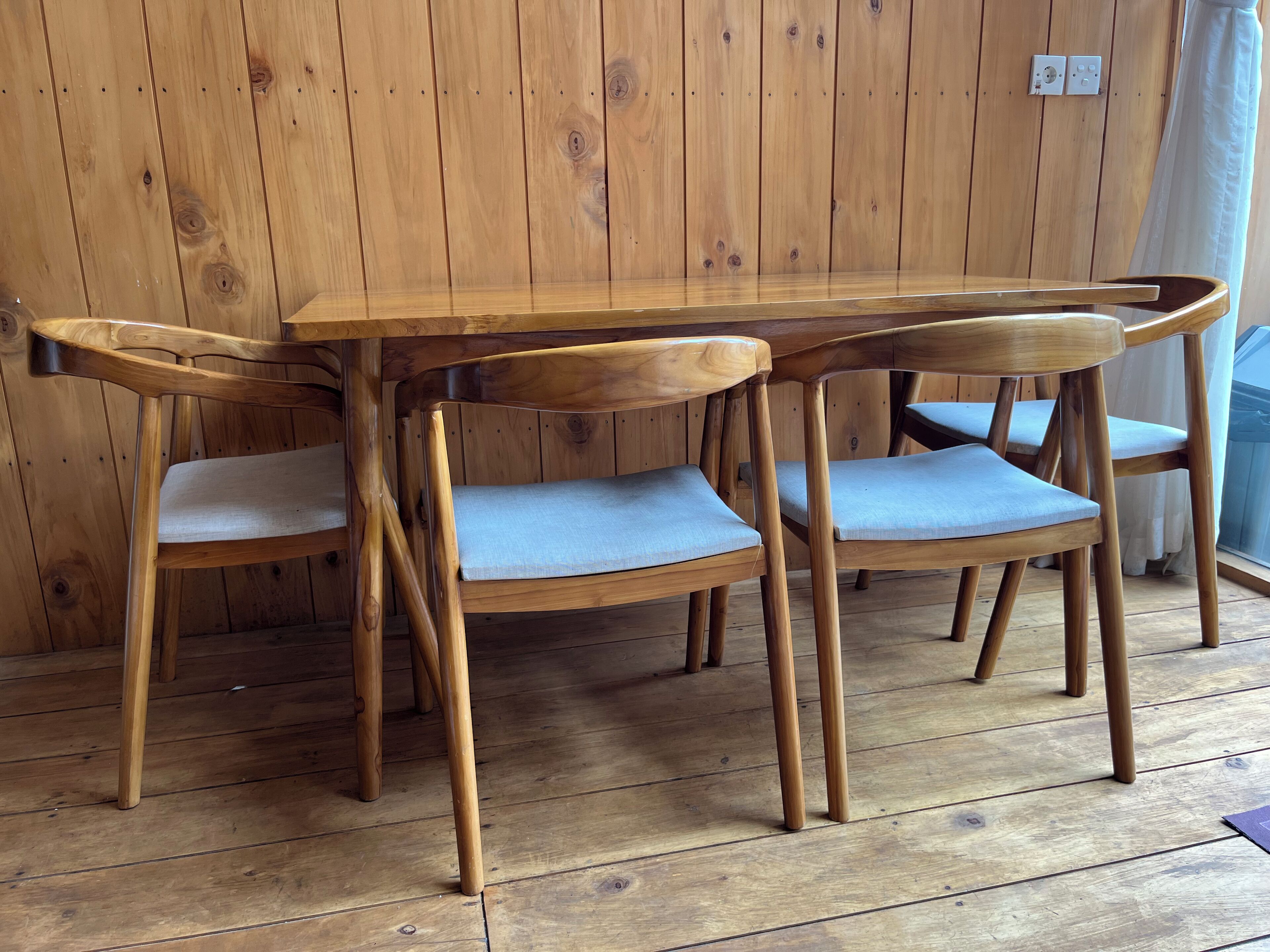 A wooden dining table with four chairs, set against a wooden wall.