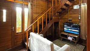 A wooden cabin interior with a staircase, a sofa, a television, and a patterned rug. - Fifa Cabin Dieng By Fifa Grup (Dieng Kulon)