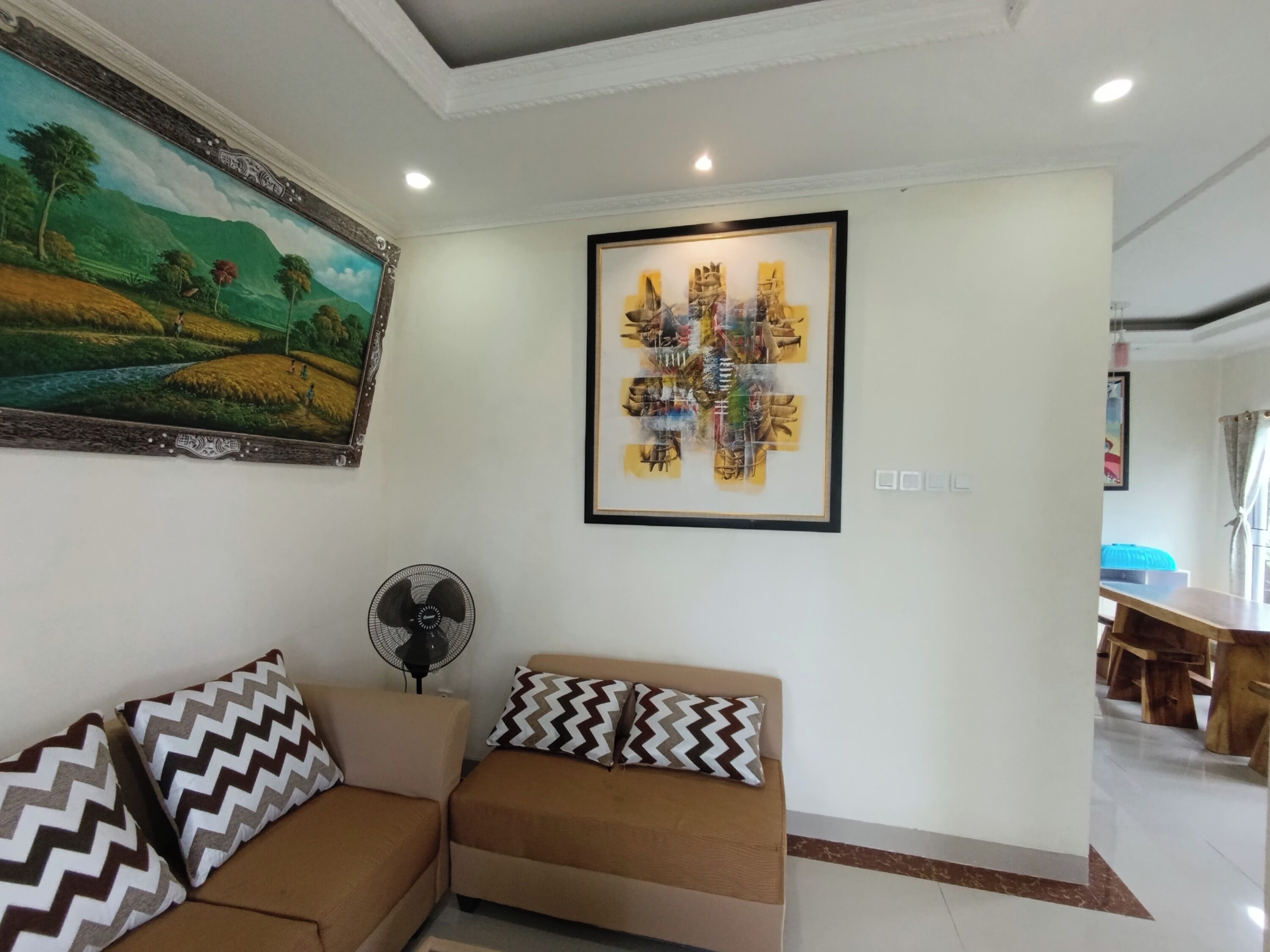 Un salon avec un canapé, un ventilateur et un tableau accroché au mur.