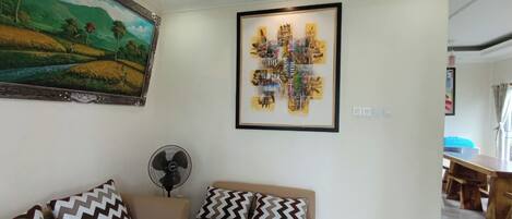 Un salon avec un canapé, un ventilateur et un tableau accroché au mur.