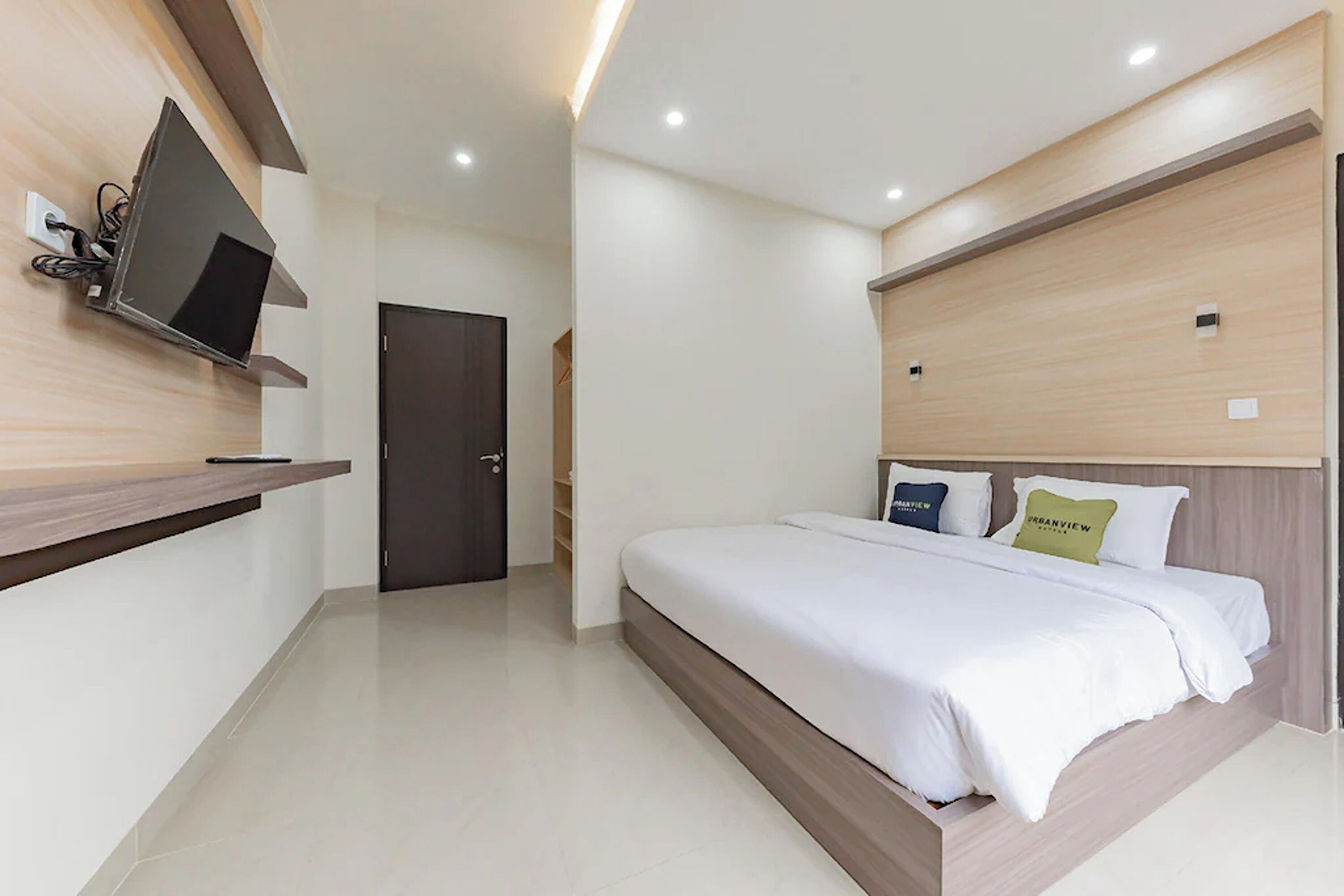 A modern hotel room with a flat-screen TV mounted on the wall, a bed with white bedding, and a wooden headboard.