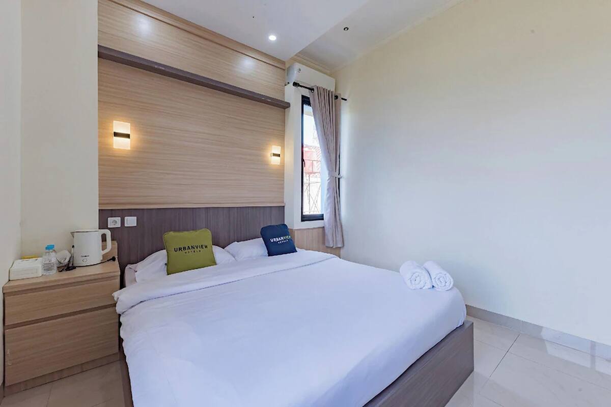 Una habitació d'hotel amb un llit gran, una tauleta de nit amb una papereta, un almoiner i una finestra amb cortines.