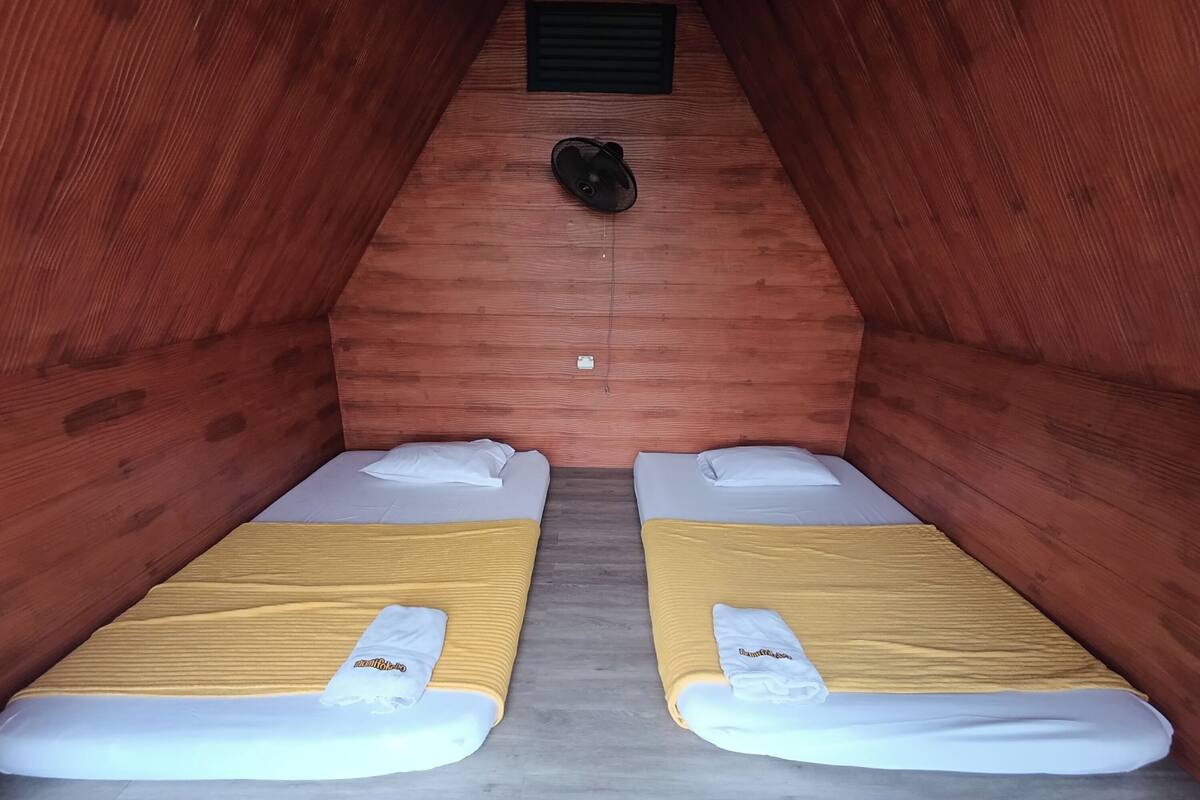 Una habitació amb dos llits, cadascun amb un estovat groc i coixins blancs, i un objecte negre a la paret.