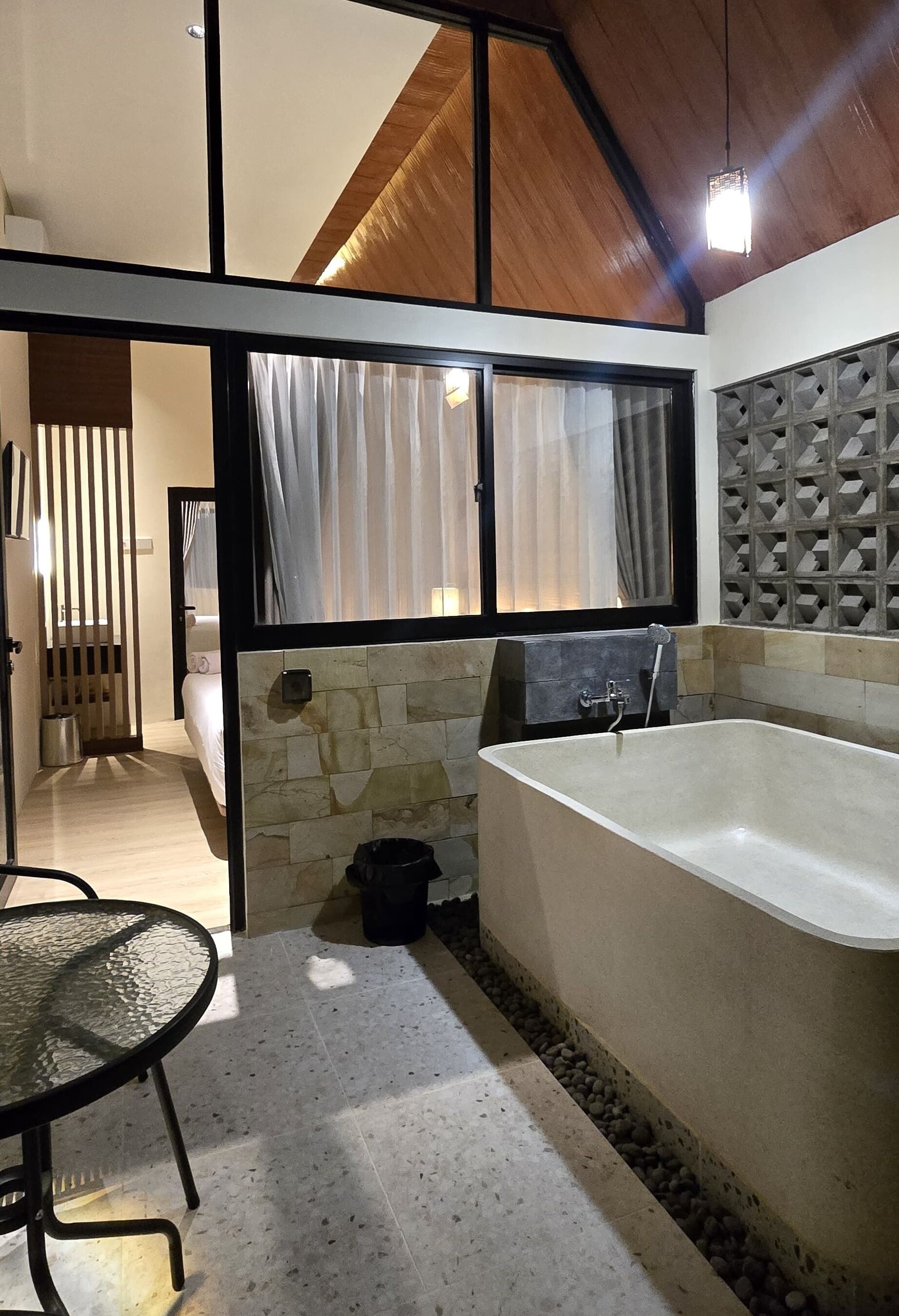 A modern bathroom with a freestanding bathtub, stone wall, and a glass partition.
