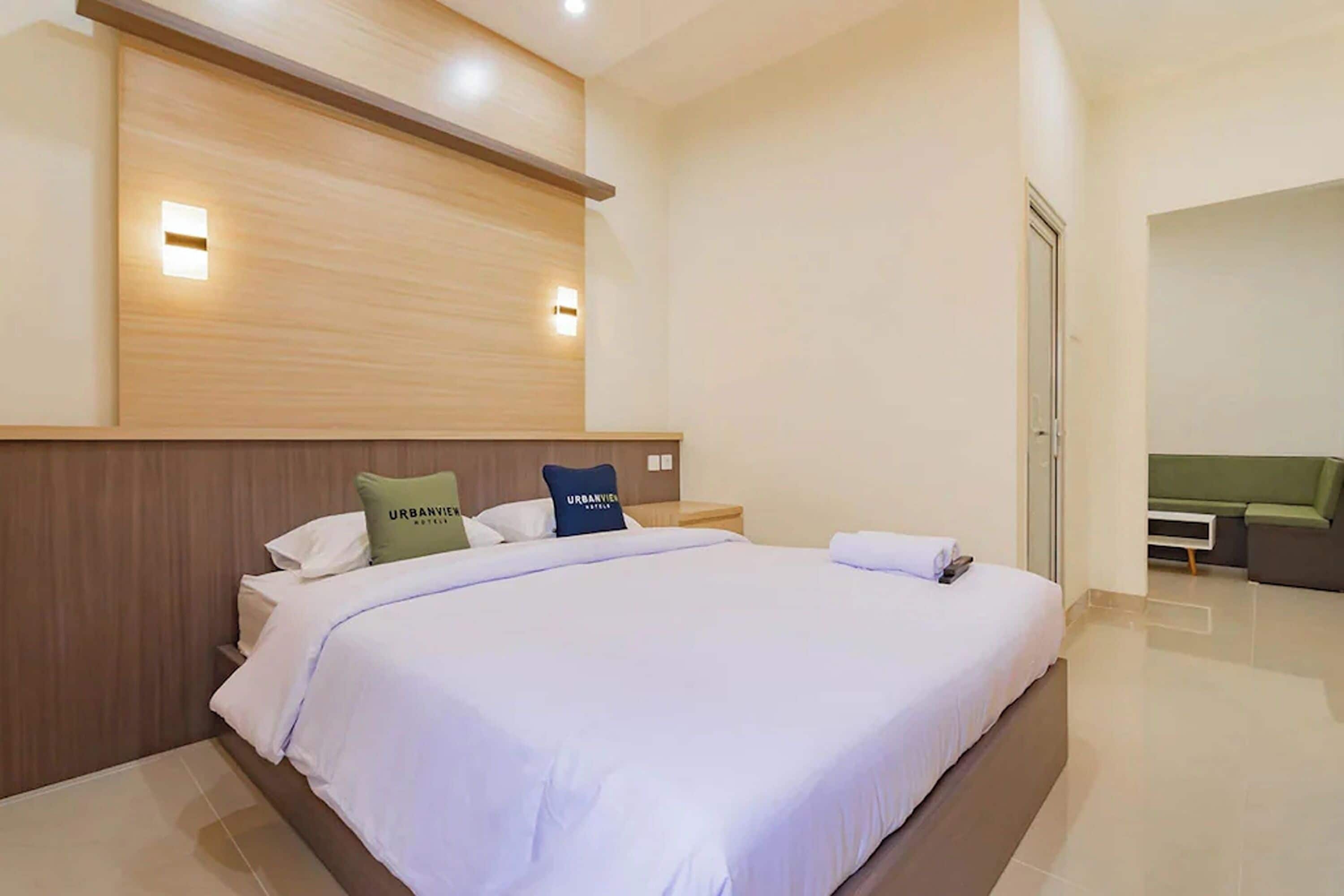 A modern hotel room with a large bed, a wooden headboard, two bedside lamps, and a green sofa in the corner.
