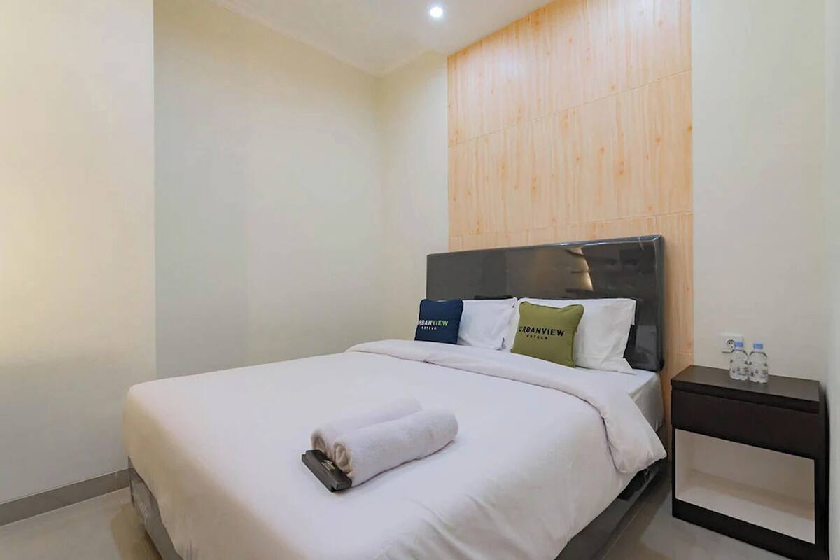 Habitació d'hotel amb llit, una tauleta de nit i un mur de panells de fusta.