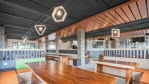 Een modern restaurant met houten tafels en banken, zeshoekige lampen en uitzicht op de omgeving.
