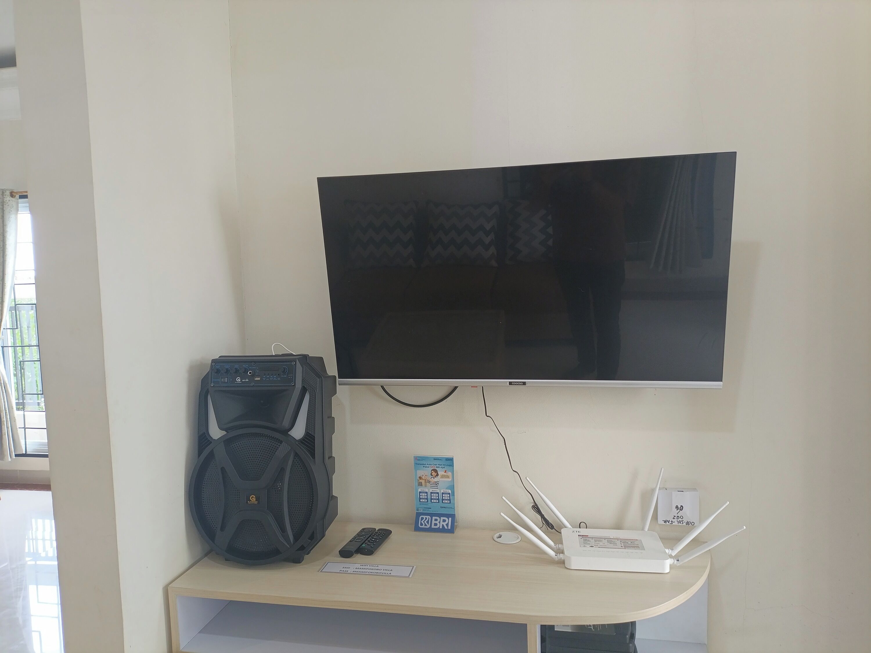 Een televisie bevestigd aan een muur, met een soundbar en een router op een bureau eronder.