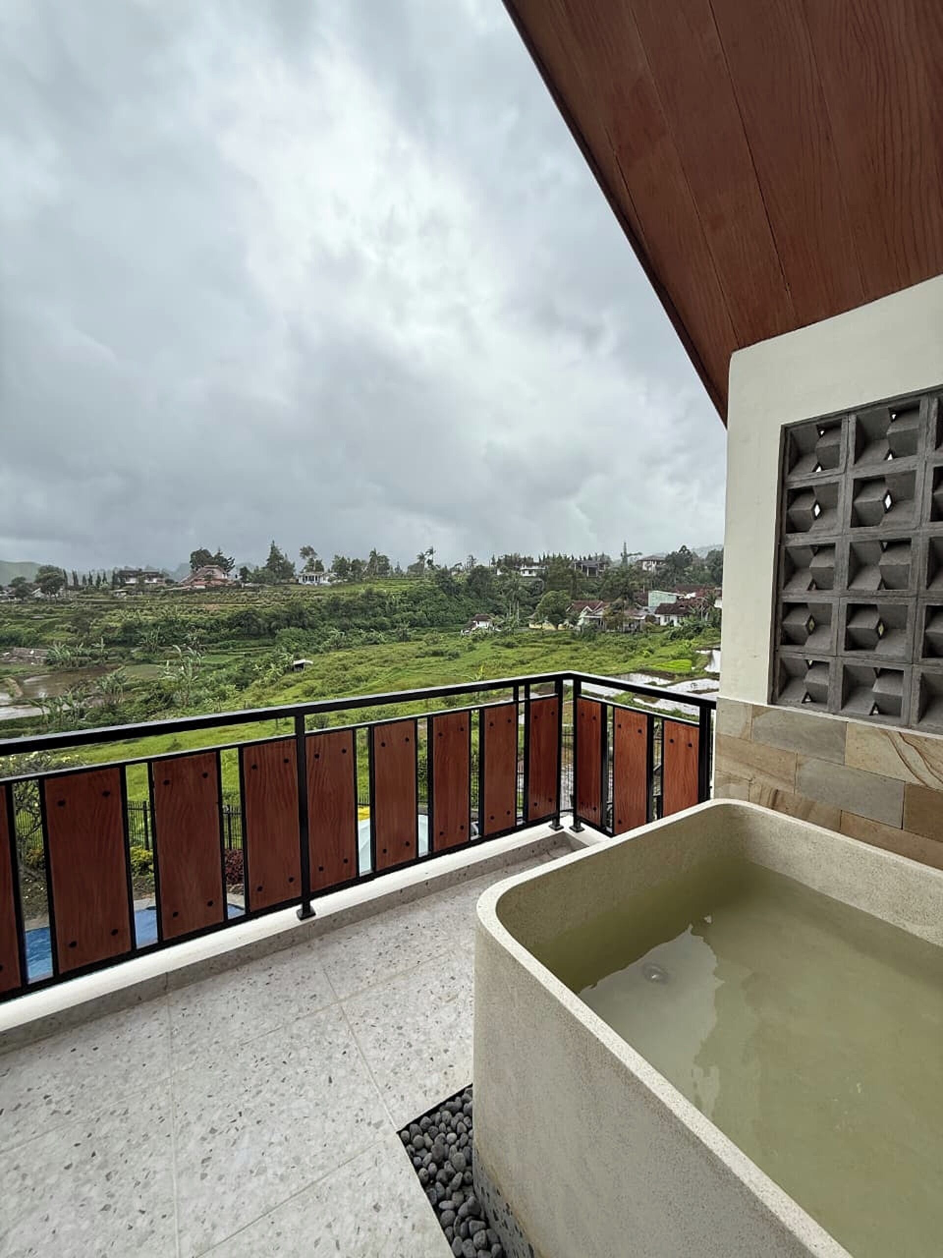 A balcony with a view of a green landscape, a wooden fence, and a spa area with a hot tub.