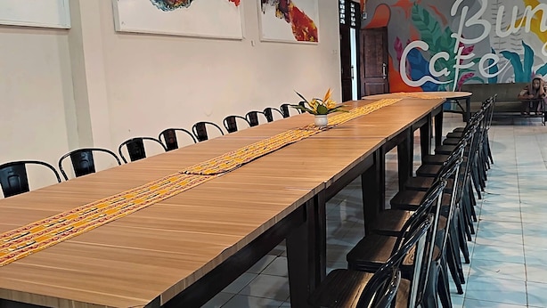 A conference room with a long wooden table, black chairs, and a colorful wall mural. - Esemka Hotel and Convention Kotabumi (Kali Balangan)