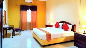 A hotel room with a bed, bedside tables, a desk, a chair, a mirror, and a window with curtains. - Esemka Hotel and Convention Kotabumi (Kali Balangan)