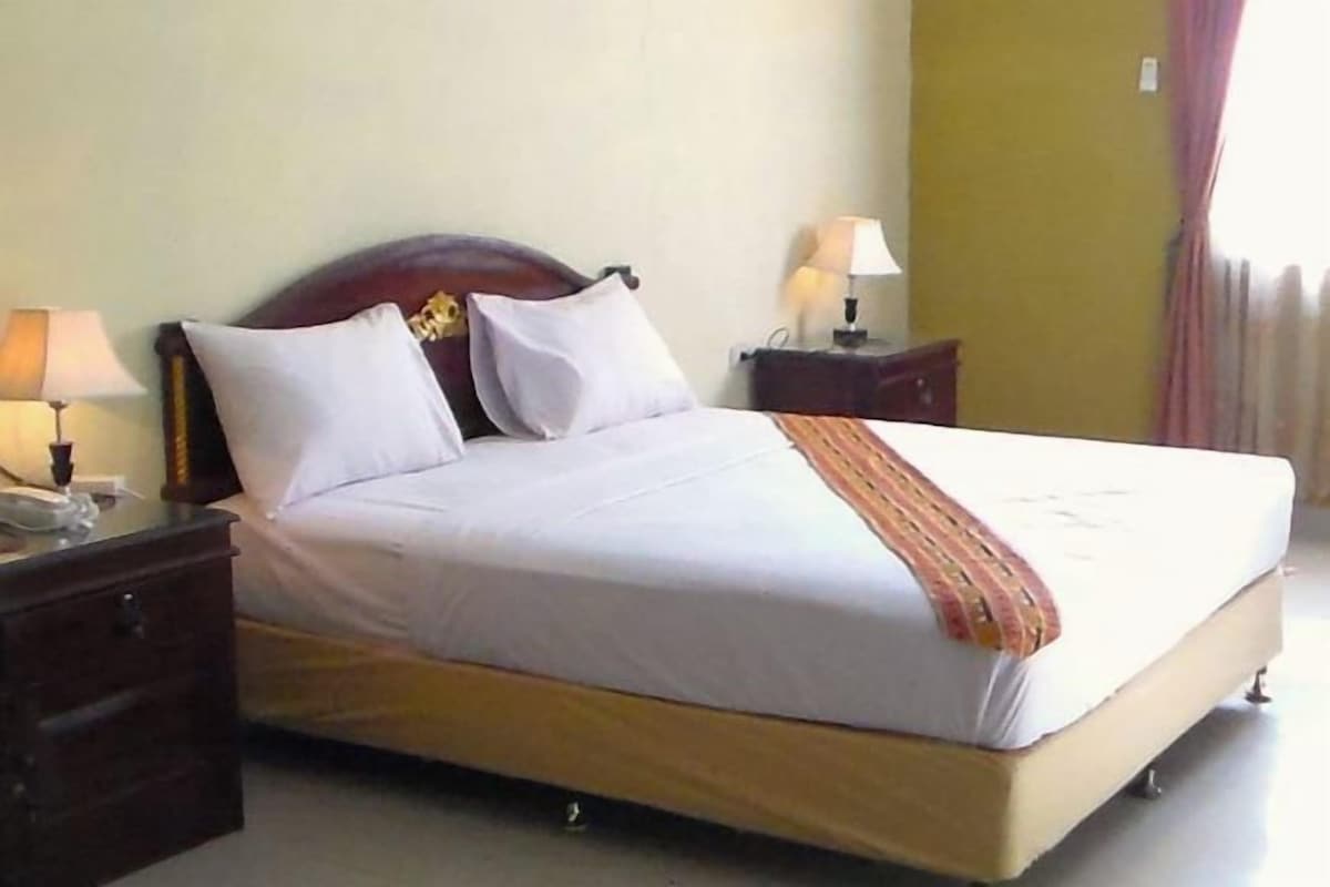 A standard hotel room with a single bed, bedside tables, and lamps.