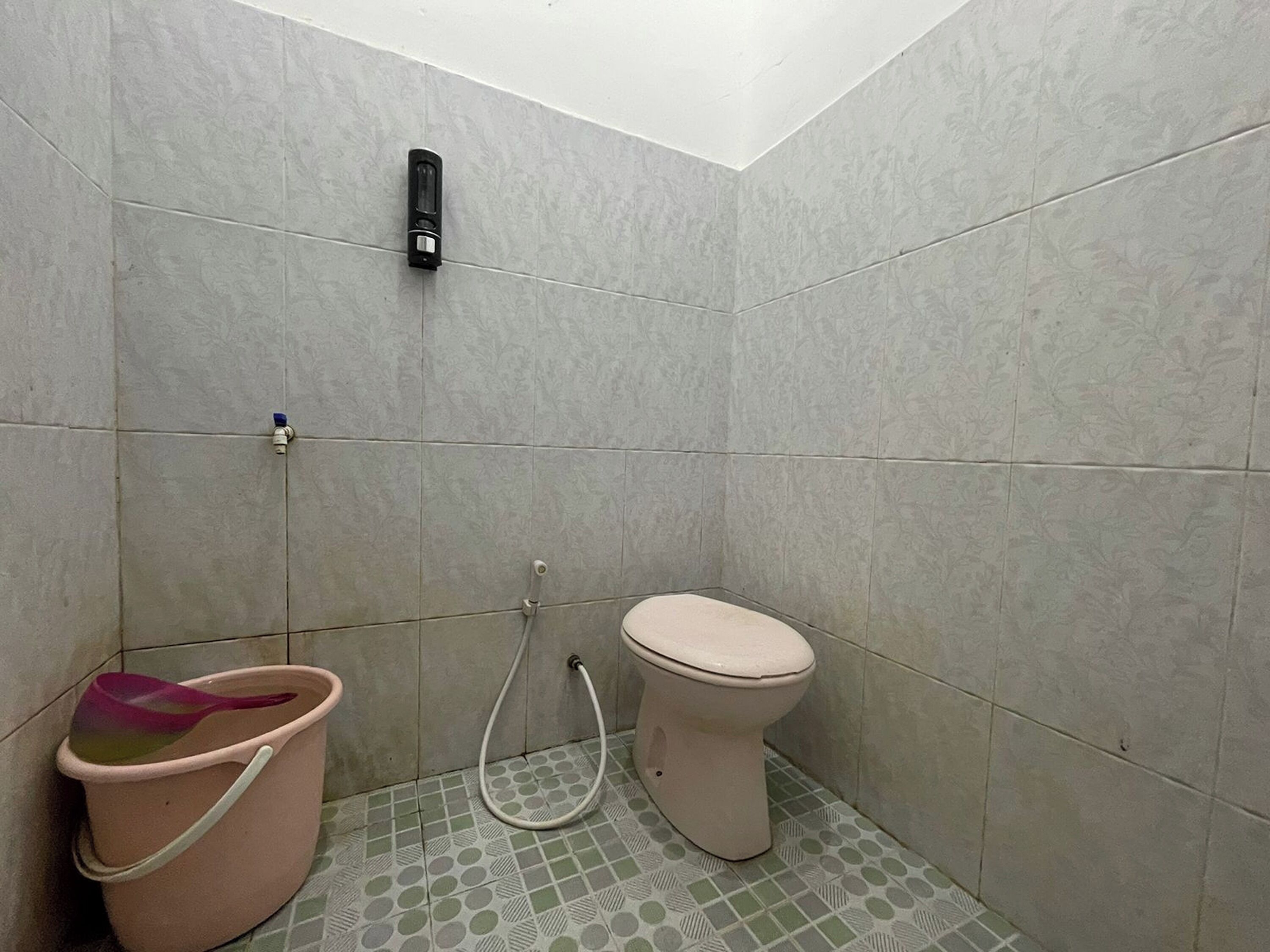 Egy kis fürdőszoba, amelyben egy WC, egy vödör és egy zuhanycső található.