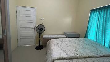 A bedroom with a bed, a standing fan, a bedside table, and a door.