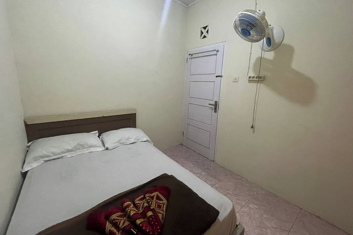 Un dormitorio pequeño y sencillo con una cama individual, un ventilador de pared y una puerta.