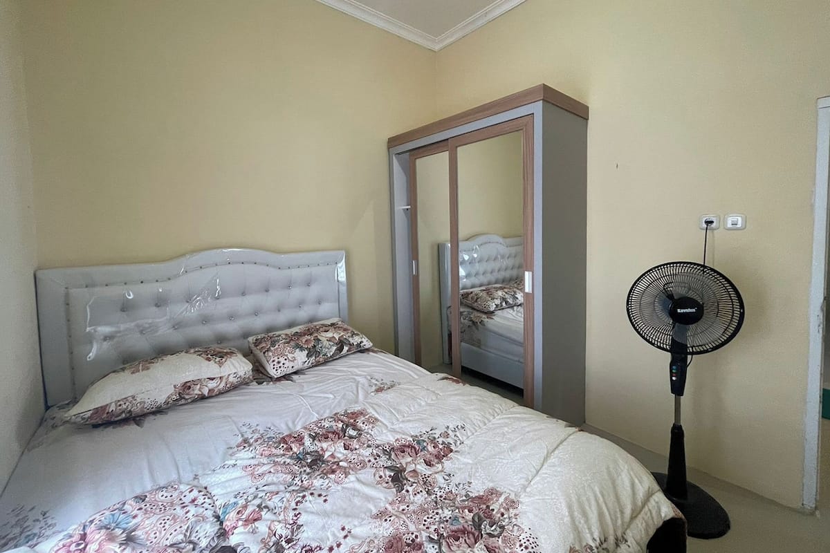 Un dormitorio con cama, armario y ventilador de pie.