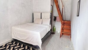 A bedroom with a bed, a wooden staircase, and a white wall. - Homestay Wong Kito (Harau)
