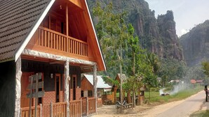 A wooden house with a balcony, surrounded by greenery and a mountainous backdrop. - Homestay Wong Kito (Harau)