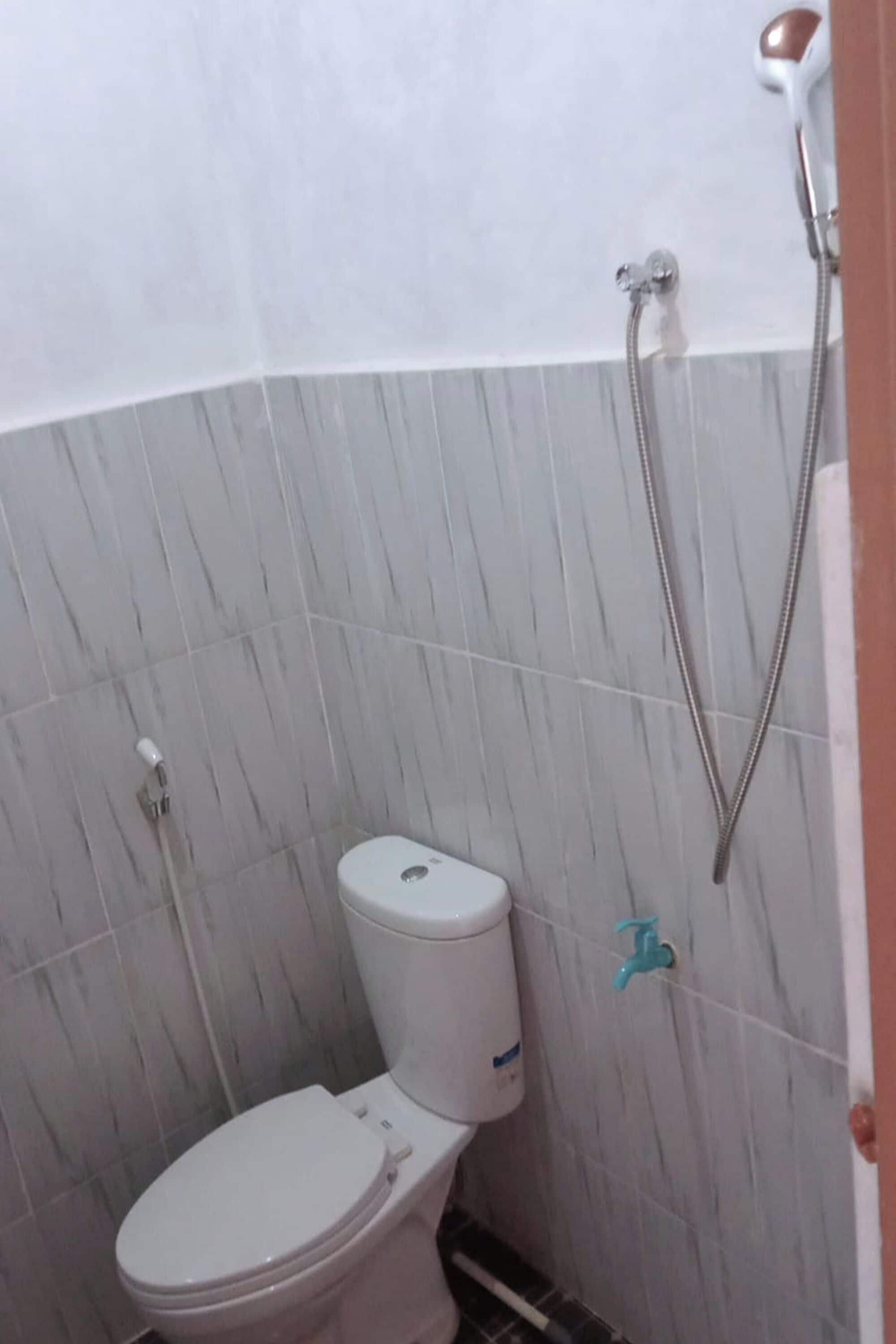 A small bathroom with a toilet, a shower, and a wall-mounted faucet.