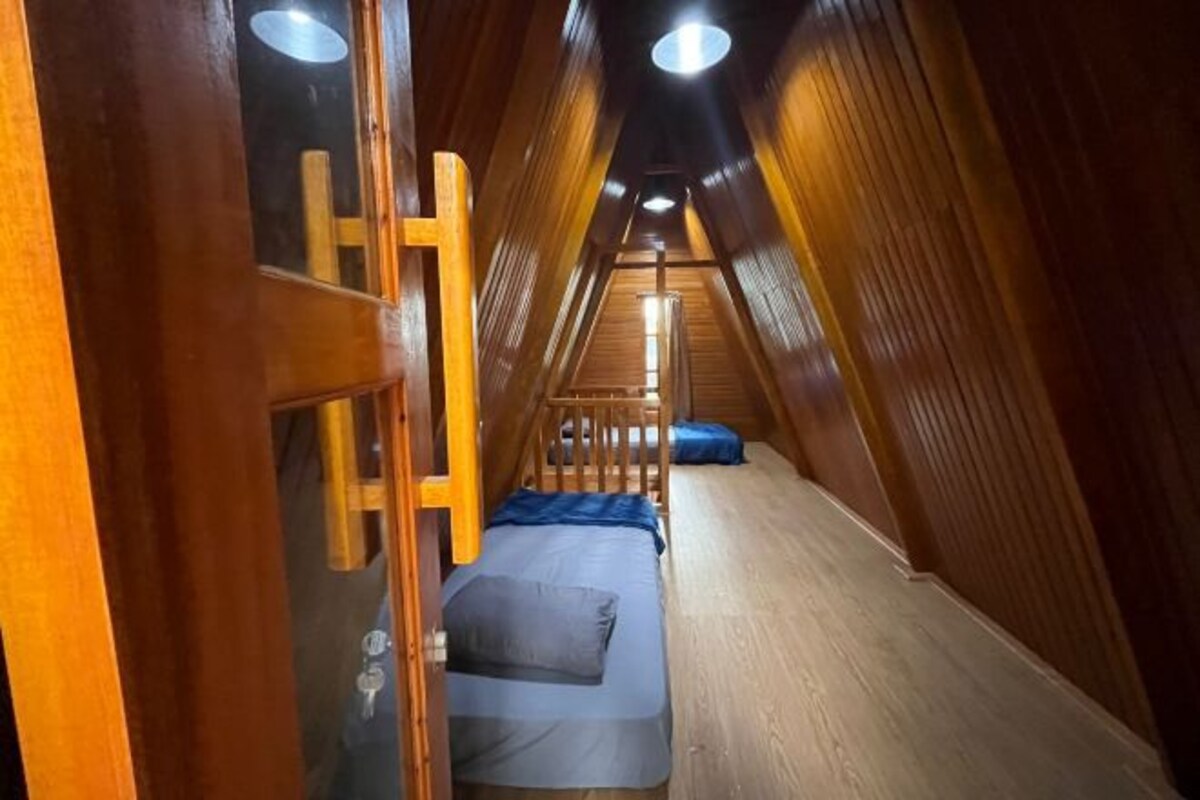 A narrow, wooden-roofed attic room with a bunk bed and a small desk.