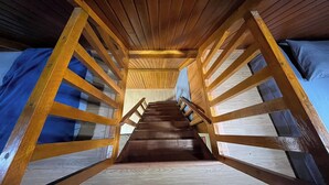 A wooden staircase with a handrail leading to a room with a blue wall and a bed. - Villa Tapian Banda (Bukittinggi)