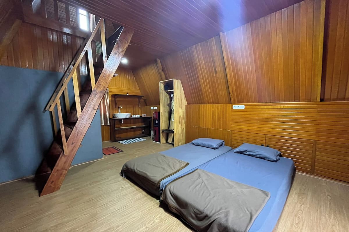 Un dormitorio cálido en el ático con una escalera de madera, dos camas con ropa de cama azul y una kitchenette pequeña.