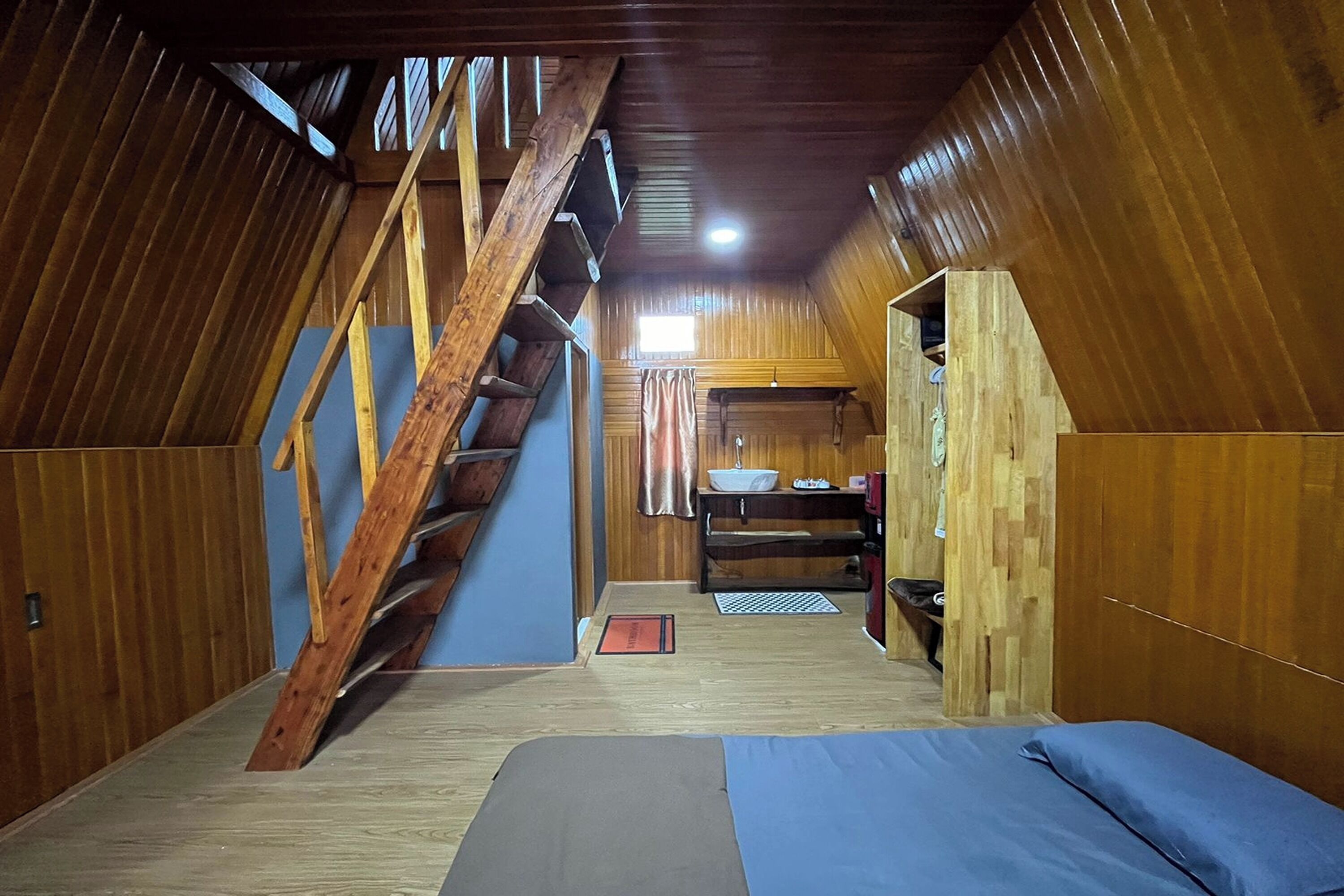 A wooden interior with a bunk bed, a wooden staircase, and a small kitchenette.