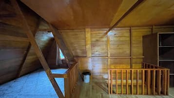 Una stanza mansardata in legno con tetto spiovente, un piccolo tavolo di legno e un cestino.