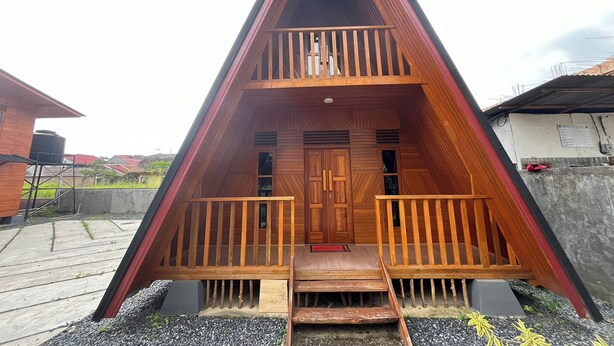 A wooden A-frame cabin with a balcony, a front door, and a small porch area. - Villa Tapian Banda (Bukittinggi)
