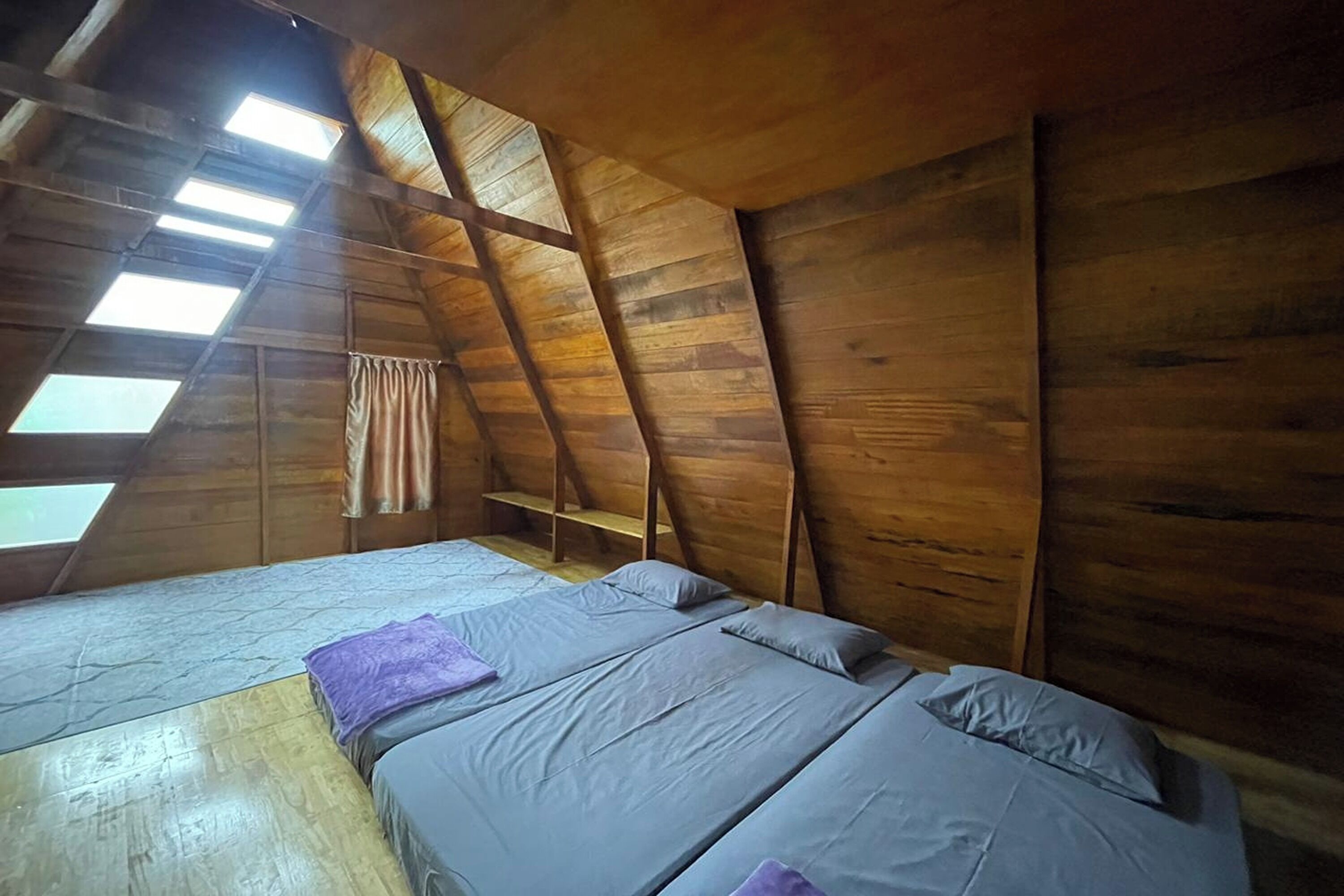 A loft-style bedroom with wooden walls and a sloped ceiling. There are two beds with gray bedding and a window providing natural light.