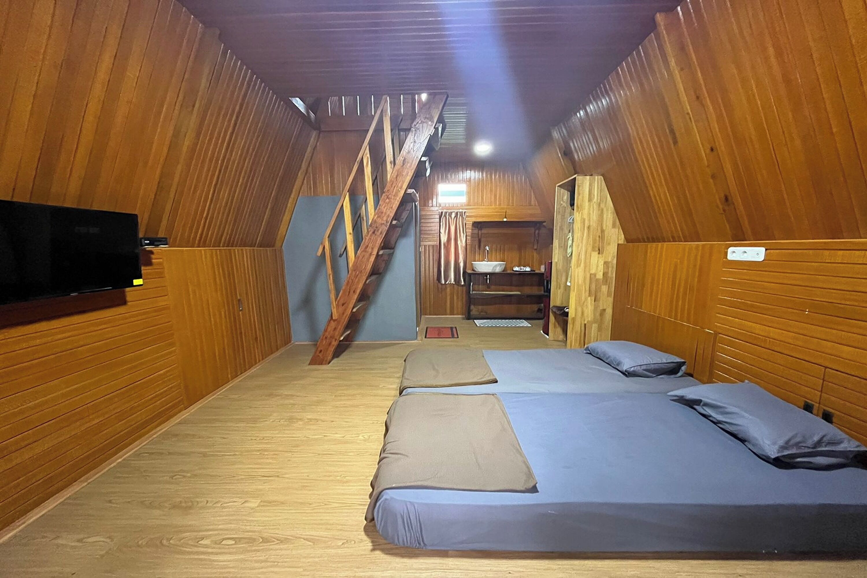 Een chalet met houten wanden, een trap en drie bedden met blauw beddengoed.