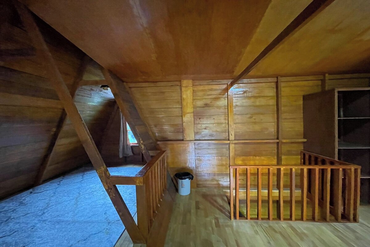 Una stanza mansardata in legno con tetto spiovente, un piccolo tavolo di legno e un cestino.