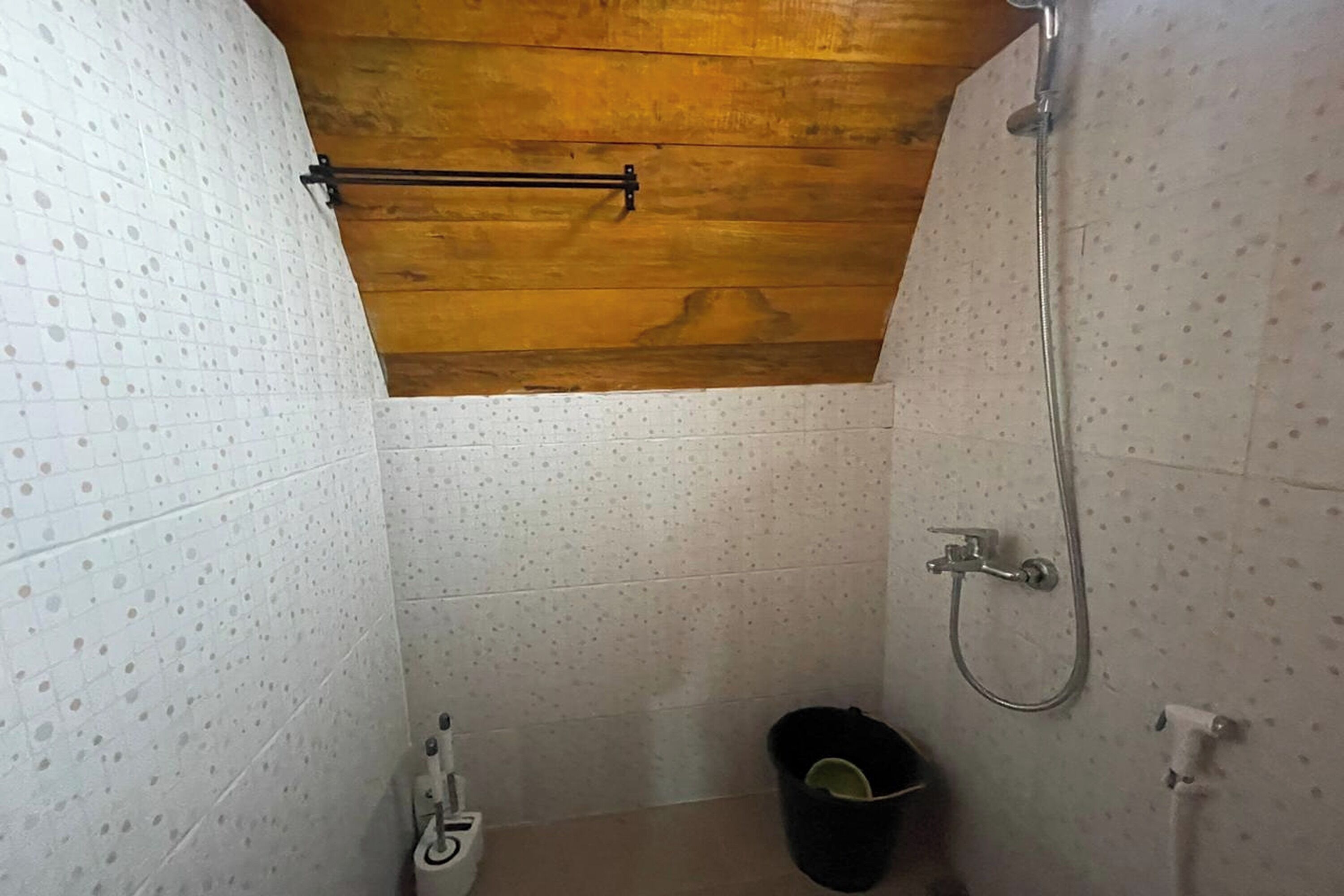 Un baño pequeño con azulejos, techo de madera, ducha y retrete.