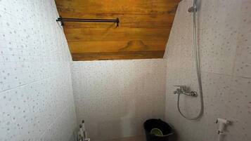 Un baño pequeño con azulejos, techo de madera, ducha y retrete.