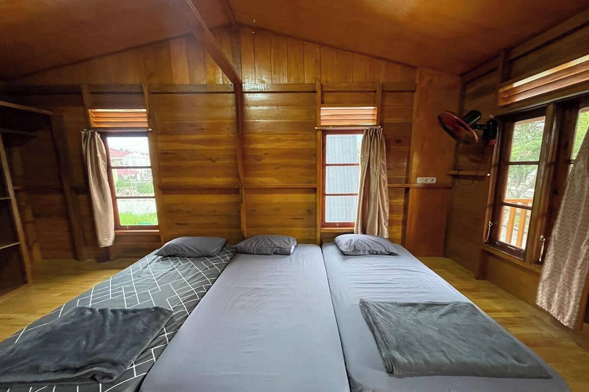 Una habitación de cabaña de madera con dos camas, un ventilador de techo y ventanas con cortinas.