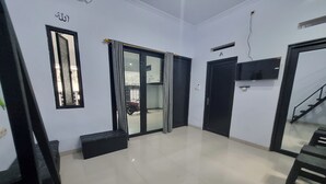 A spacious living room with a large sliding glass door, a black sofa, a black ottoman, and a flat-screen TV mounted on the wall.