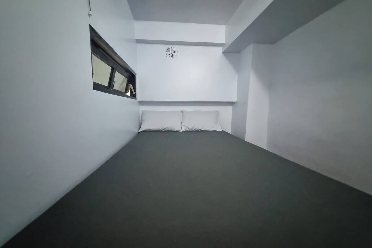 A room with a bed, a window, and a wall-mounted light fixture.