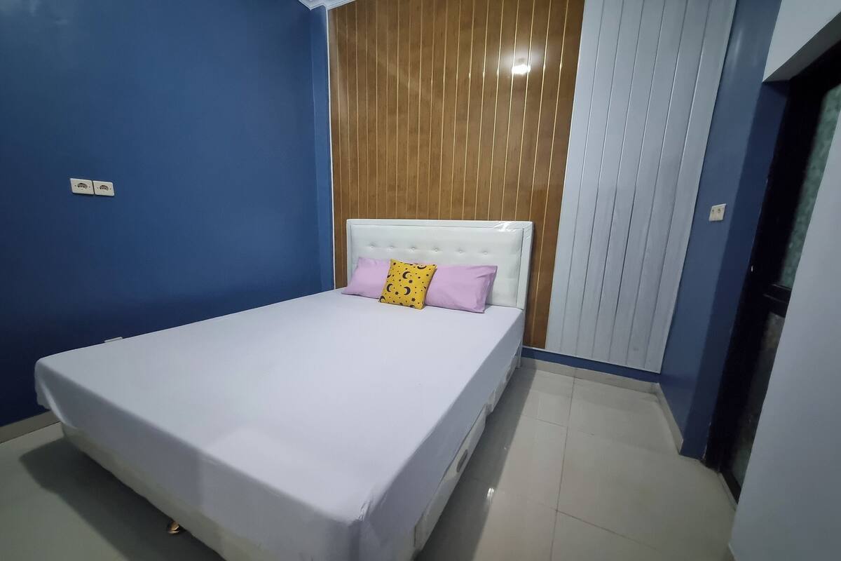 A bedroom with a white bed, a blue wall, and a wooden panel wall.