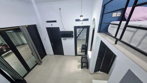 A compact hotel room with a bunk bed, a small desk, and a mirror. There is a door leading to another room and a staircase visible in the background.