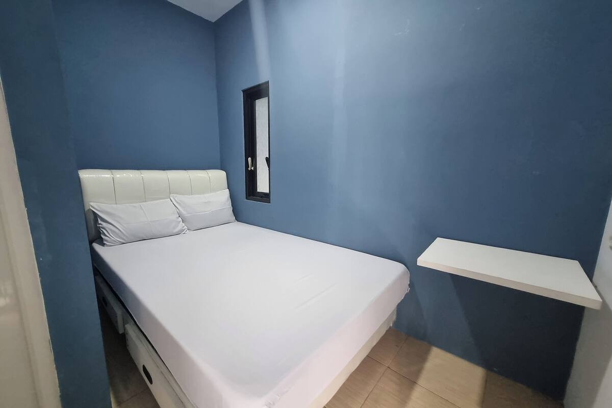 A bedroom with a bed, a white headboard, a small window, and a white shelf.