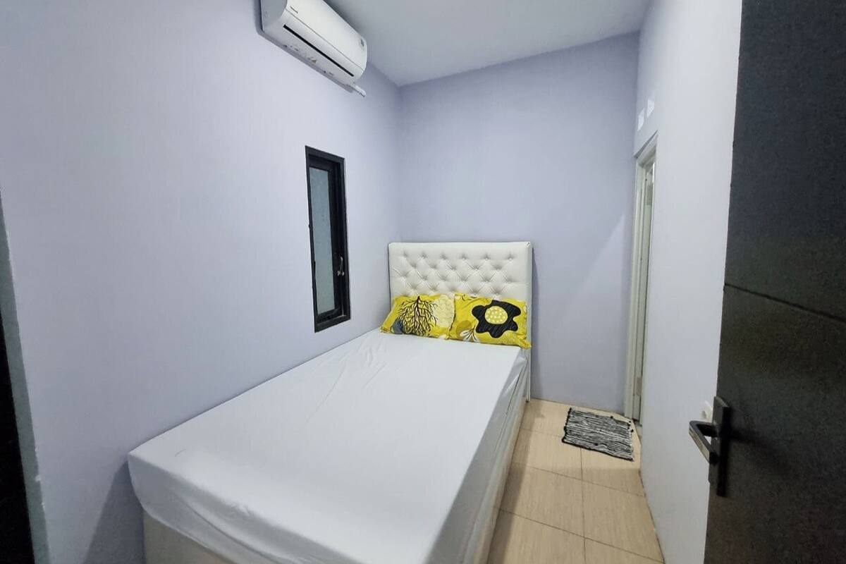 A small, neatly arranged bedroom with a single bed, a window, and an air conditioning unit.