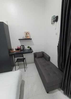 A small, modern room with a bed, a desk, a chair, a sofa, and a wall-mounted TV. - House Of Marvilla (Depok)