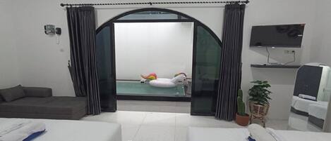 A hotel room with two beds, a TV, a small pool with a swan float, and a cactus plant.