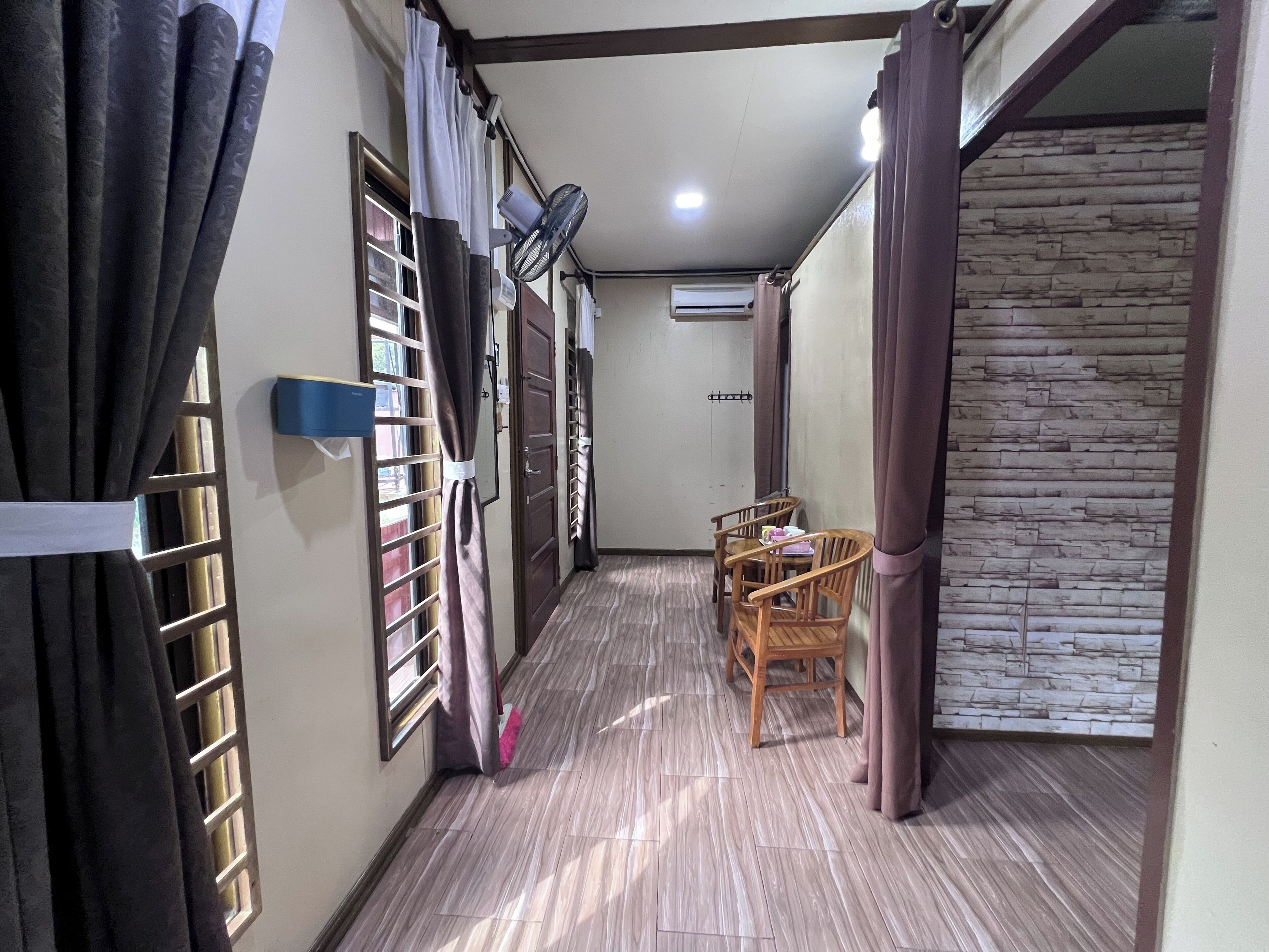 A corridor with a dining area featuring a table and chairs, a window with blinds, and a wall-mounted air conditioner.