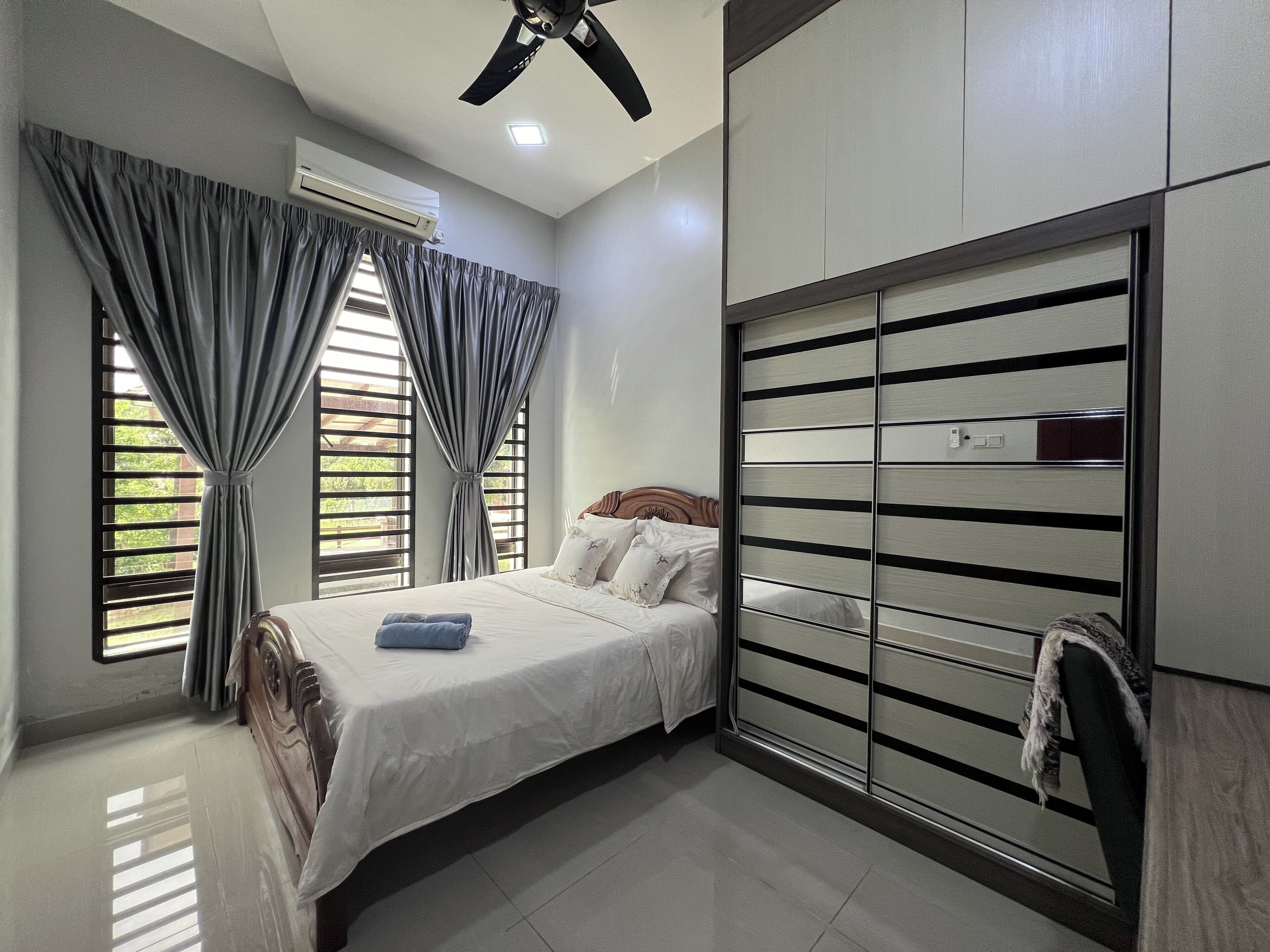A bedroom with a bed, a ceiling fan, an air conditioning unit, and a wardrobe with horizontal stripes.