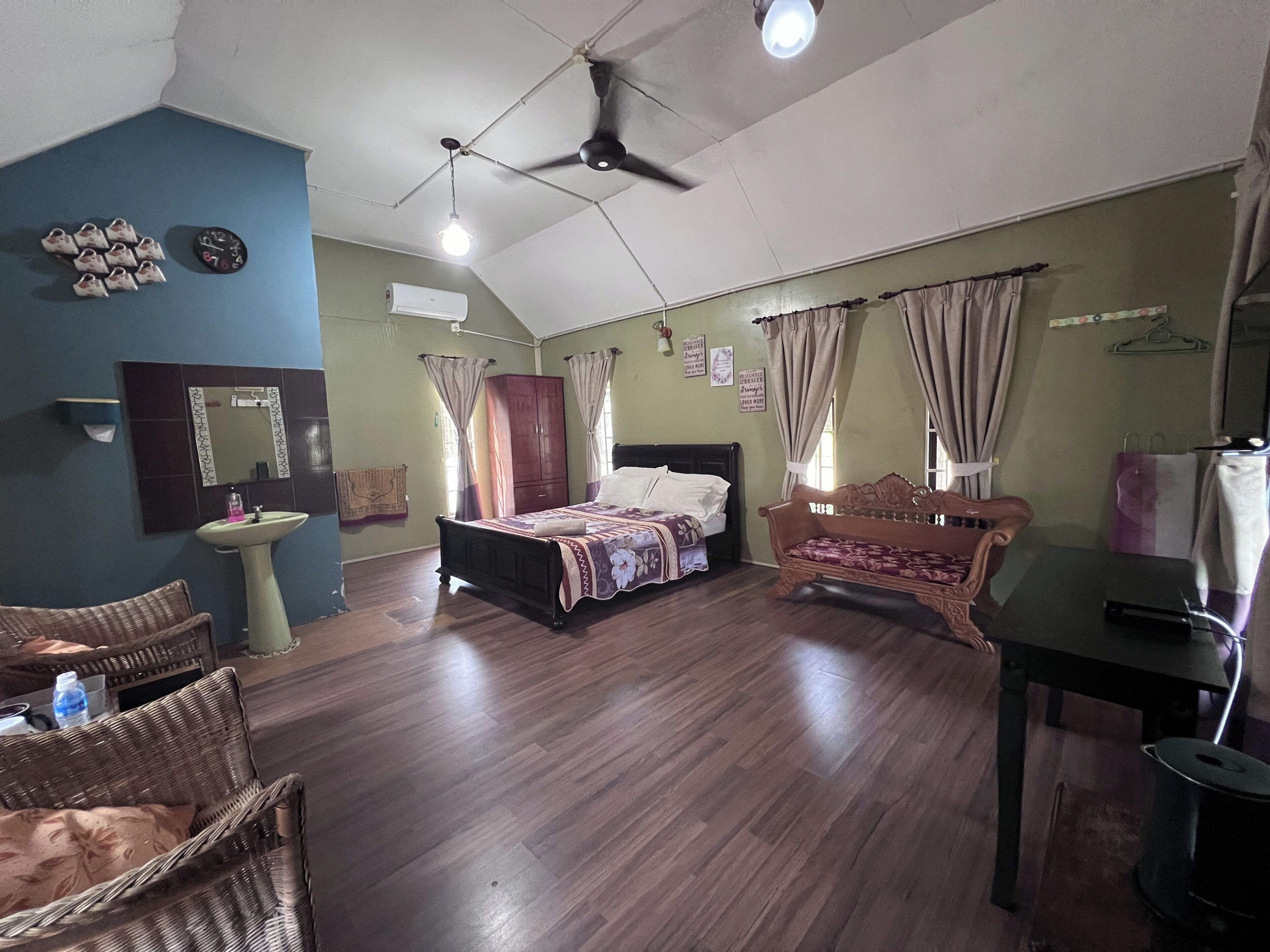 A bedroom with a bed, a wardrobe, a bedside table, a chair, a sofa, a table, a mirror, a clock, and an air conditioning unit.