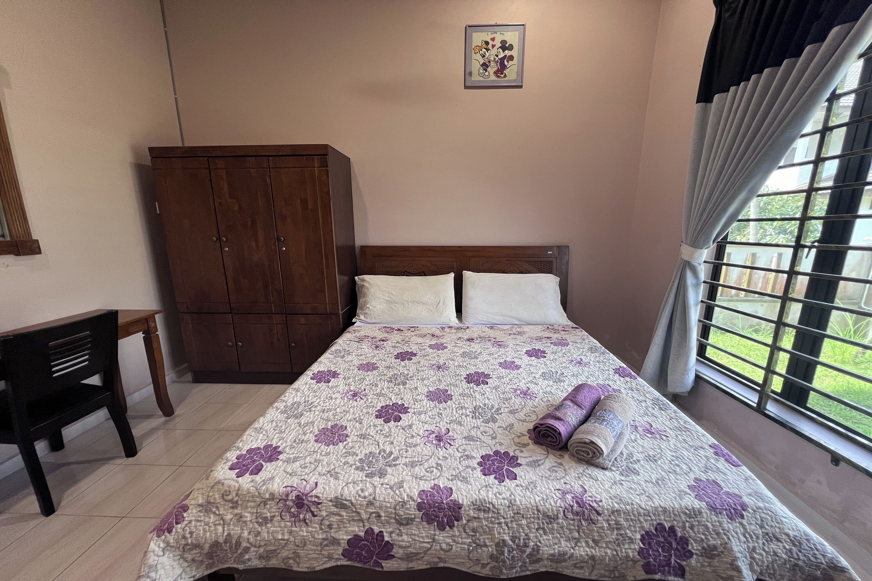 Ein Schlafzimmer mit einem Bett, einem Holzschrank, einem Schreibtisch und einem Fenster mit Vorhängen.