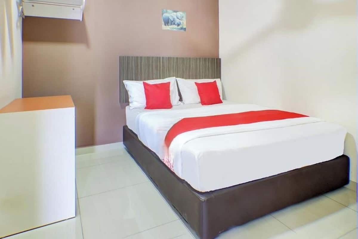Habitación de hotel con cama, mesita de noche, aire acondicionado de pared y un pequeño cuadro en la pared.