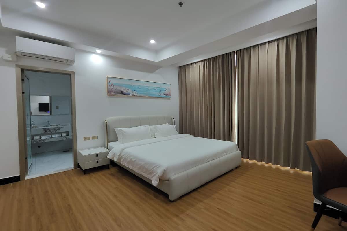 Una habitación de hotel moderna con una cama grande, una mesita de noche, una silla y un baño visible a través de una puerta abierta.
